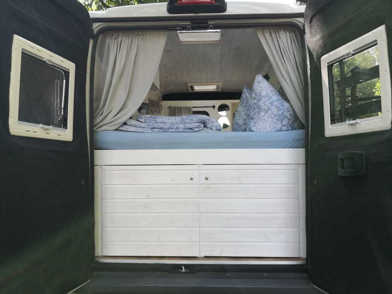 Camper Van Olaf - Heckansicht mit offener Tür und Sicht auf Bett und geschlossenem Stauraum